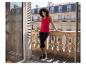 Vrouw in rood hemdje en zwarte capri-legging op een balkon met stenen balustrade.