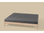 Een houten bedframe met een donkergrijs hoeslaken op een lichtbeige achtergrond.