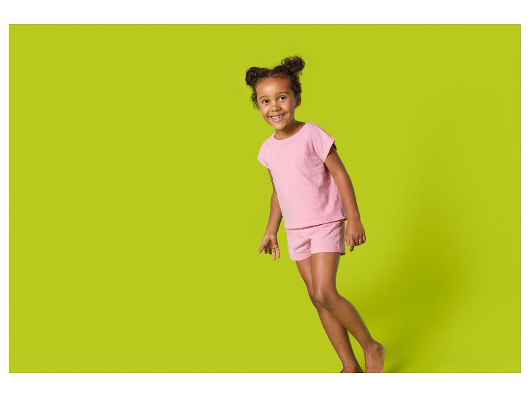 Lachend meisje in roze pyjama met stippen, staand tegen een groene achtergrond.