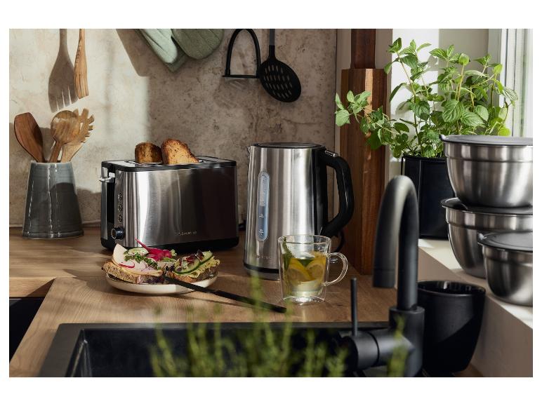 Een roestvrijstalen broodrooster en waterkoker op een houten aanrecht, met toast en thee.