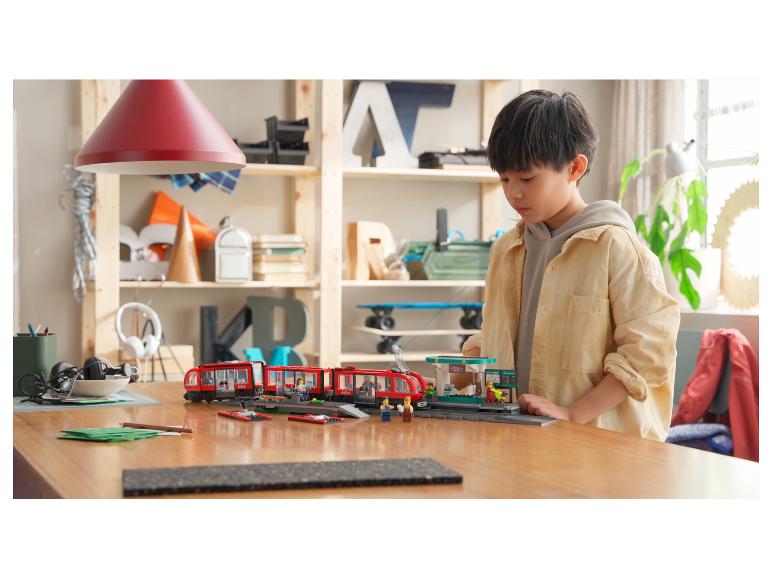 Een kind speelt met een LEGO City trein en station op een houten tafel.