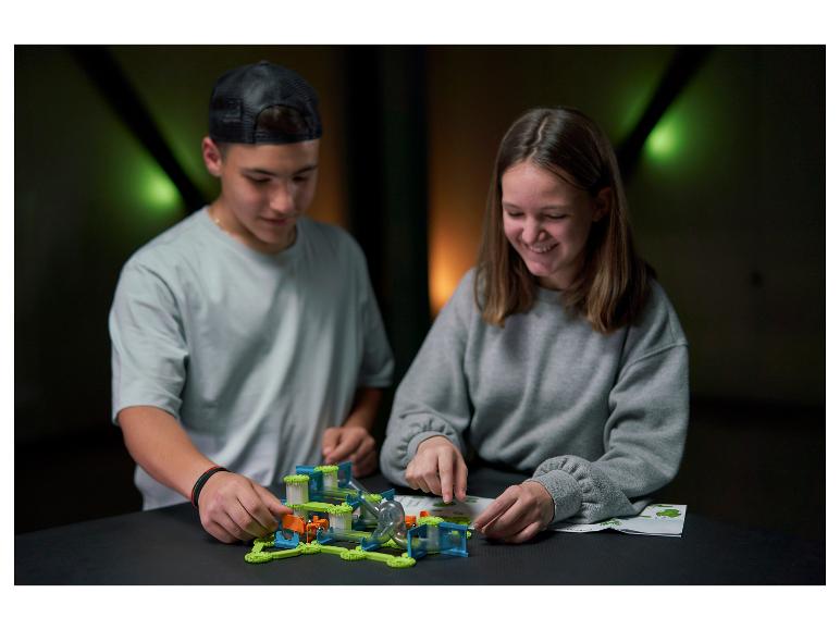 Twee kinderen bouwen een knikkerbaan, geconcentreerd op de instructies.