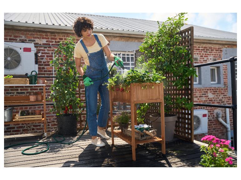 Een persoon die aardbeiplanten water geeft in een verhoogde houten plantenbak op een dakterras.