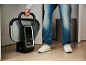 Persoon houdt een draagbare kledingstomer met digitaal display vast, draagt jeans en sneakers.