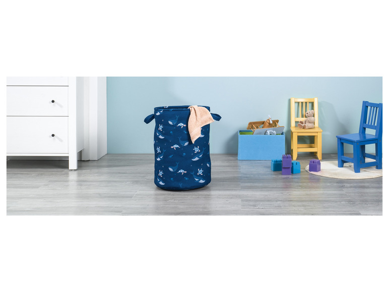 Een blauwe wasmand met walvissen en schildpadden, twee stoelen en blokken in een kinderkamer.