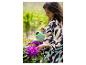 Vrouw giet paarse rododendrons water met een groene gieter.