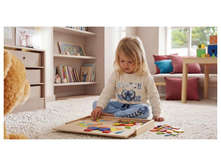 Kind speelt met een houten geometrische vormenpuzzel op een tapijt.