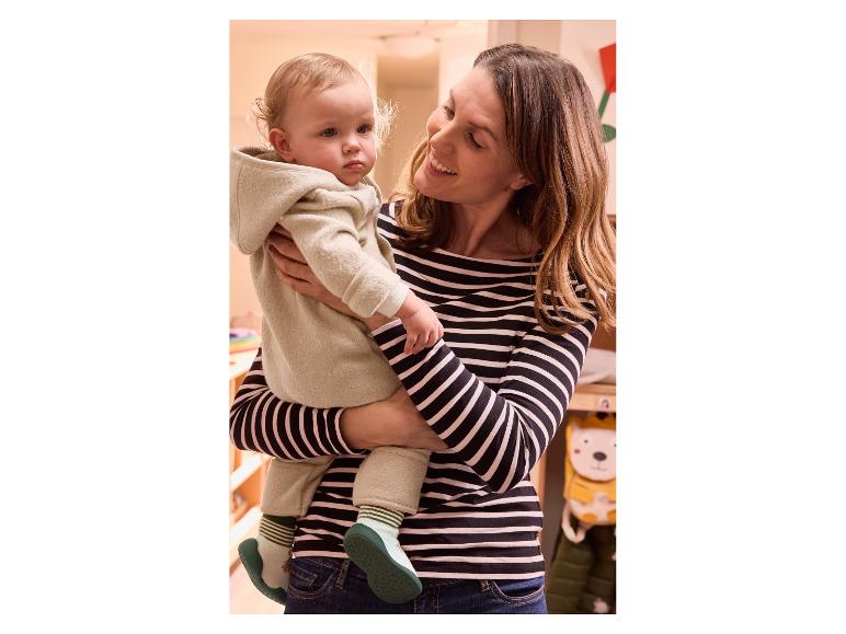 Een moeder houdt een baby vast in een lichtbeige jumpsuit.