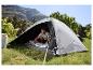 Man in grijze tent, bereidt slaapzak voor in berglandschap.