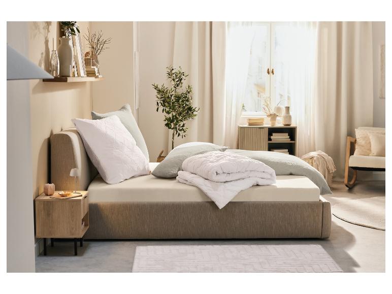 Crèmekleurig beddengoed en dekbed op een bed in een minimalistische slaapkamer.