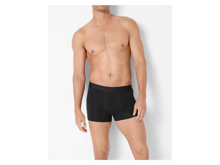 Bovenlichaam van een man in zwarte boxershorts tegen een witte achtergrond.