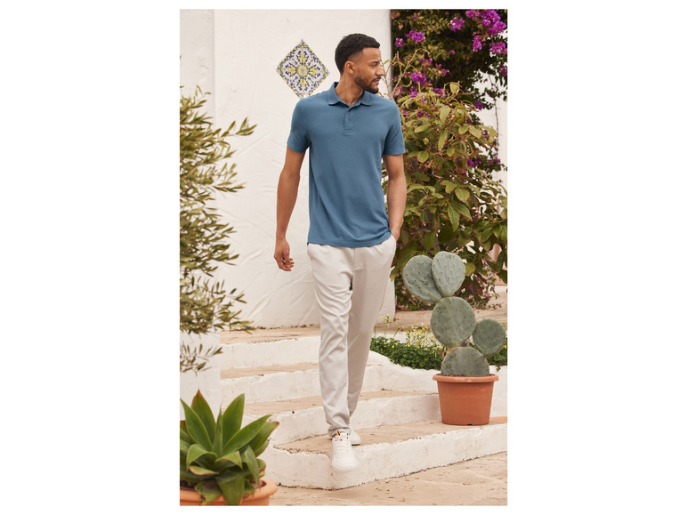 Man in een blauwe polo en beige broek loopt langs een cactus.