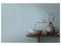 Houten tafel met decoratieve vazen, kommen en gedroogde takken tegen een blauwe muur.