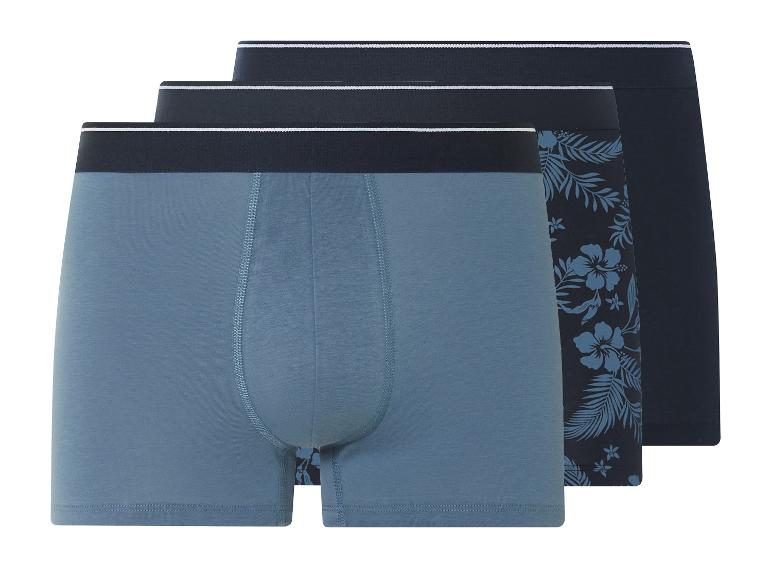Drie heren boxershorts: effen blauw, effen donkerblauw en bloemenprint.
