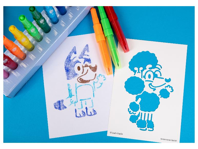 Kleurrijke krijtjes in een houder met twee stripfiguren getekend op papier.