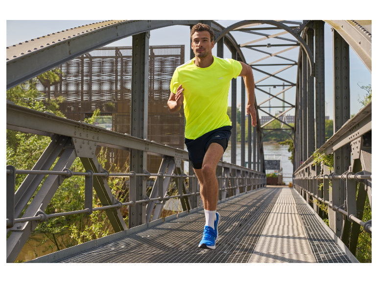 Man rent over een brug in een geel shirt en blauwe hardloopschoenen.