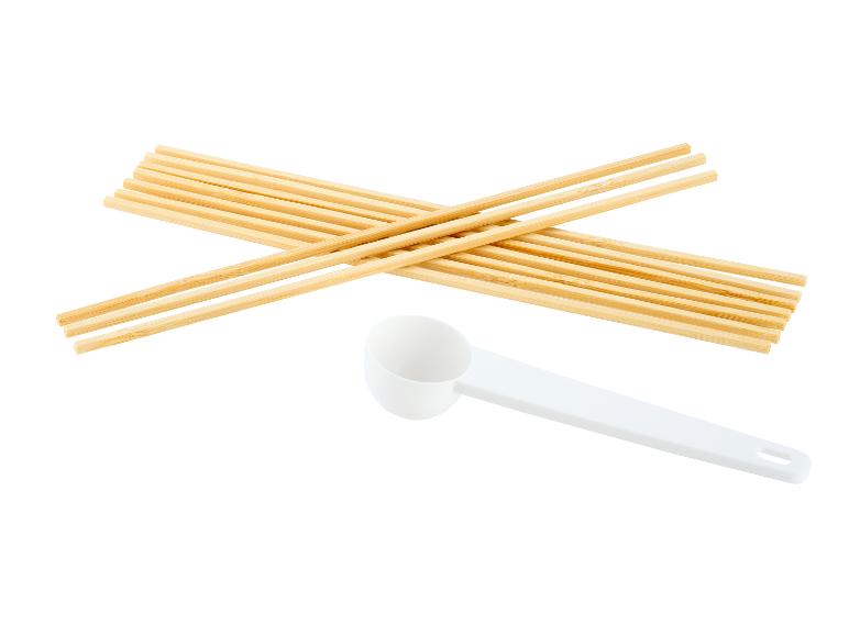 Houten stokjes en een witte maatlepel op een witte achtergrond.