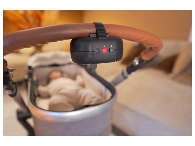 Een zwart ZAZU-apparaat is bevestigd aan de bruine handgreep van een kinderwagen met een baby.