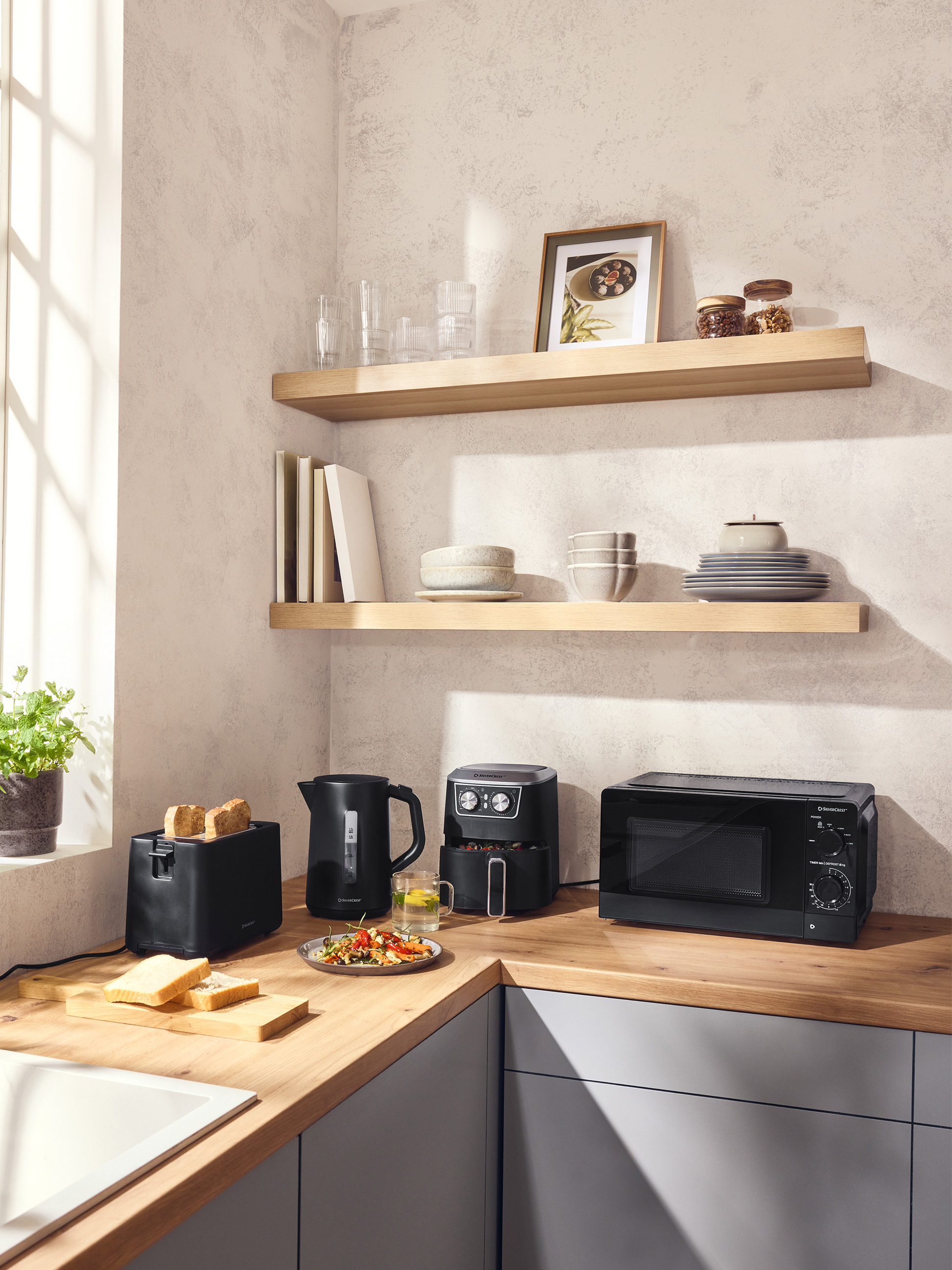 Moderne keuken met zwarte broodrooster, waterkoker, airfryer en magnetron op een houten aanrecht.