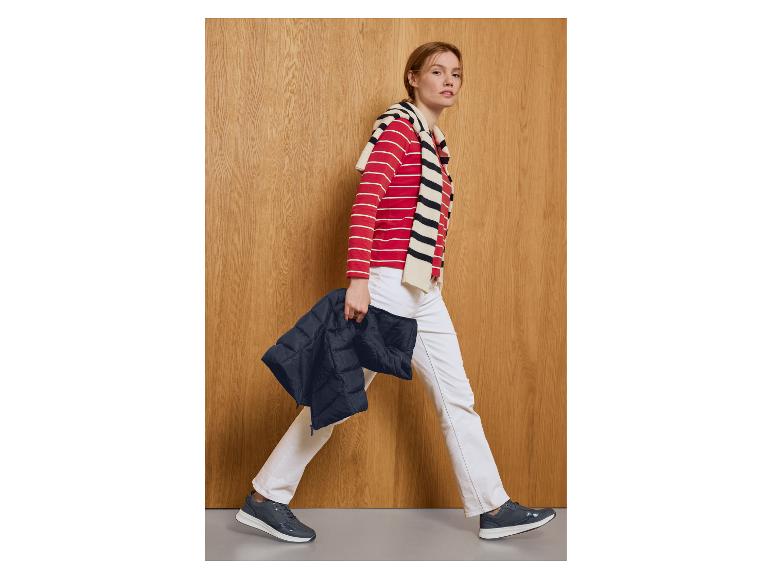 Vrouw in witte broek en rood gestreept shirt draagt een donkerblauwe gewatteerde jas.