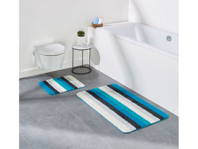 Badkamer met bad, toilet en twee badmatten met blauwe strepen.