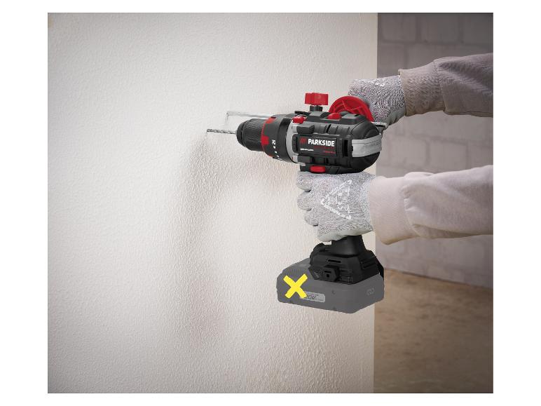 Accuboormachine met accu, boort in een witte muur met werkhandschoenen.