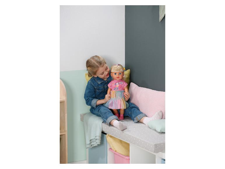 Meisje in spijkeroutfit speelt met een pop in een roze jurk op een bankje.