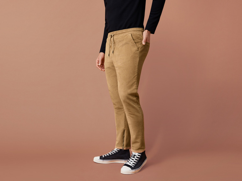 Een man draagt ​​een beige broek met een trekkoord en zwarte sneakers.