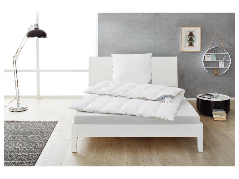 Wit bed met dekbed en kussen, leeslamp en bijzettafel in een moderne slaapkamer.