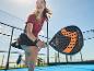 Vrouw speelt padel, met een zwart-oranje padelracket.