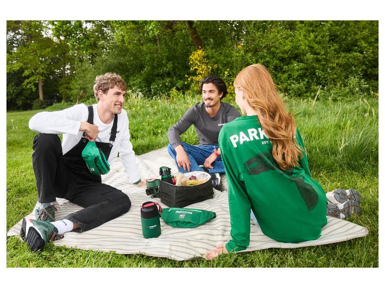 Drie vrienden picknicken op het gras met groene koeltassen en waterflessen.