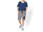 Een jongen draagt een blauwe T-shirt, grijze Jurassic World shorts en blauwe sneakers.