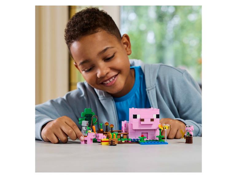 Een lachende jongen speelt met een LEGO Minecraft varkensboerderijset.