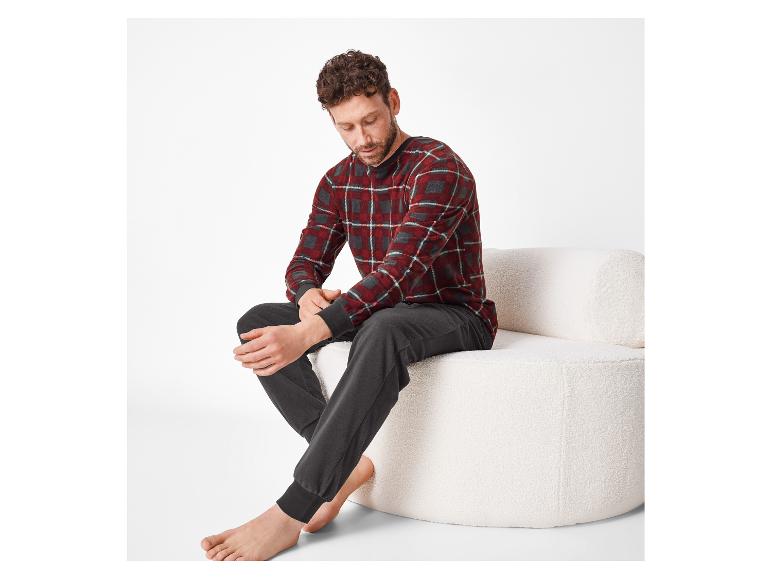 Man in rood geruite pyjama en grijze broek, zittend op een witte bank.