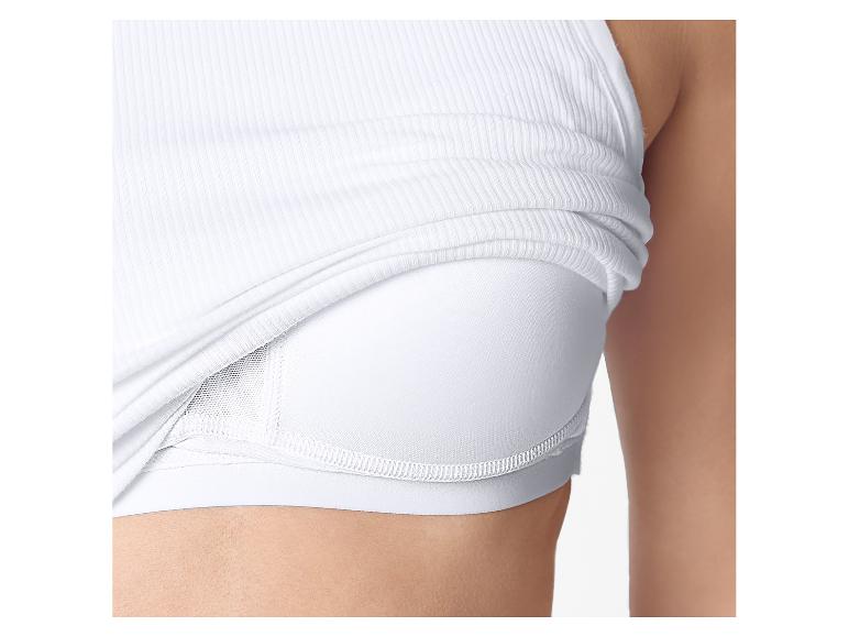 Close-up van een vrouw met een witte geribbelde tanktop over een witte sportbeha.