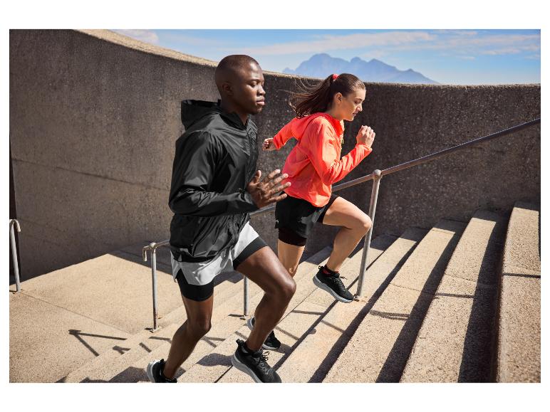 Twee atleten in sportkleding rennen buitentrap op met bergen op de achtergrond.