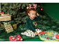 Een peuter in een feestelijke pyjama zit bij een kerstboom met cadeautjes en een Grinch-kussen.