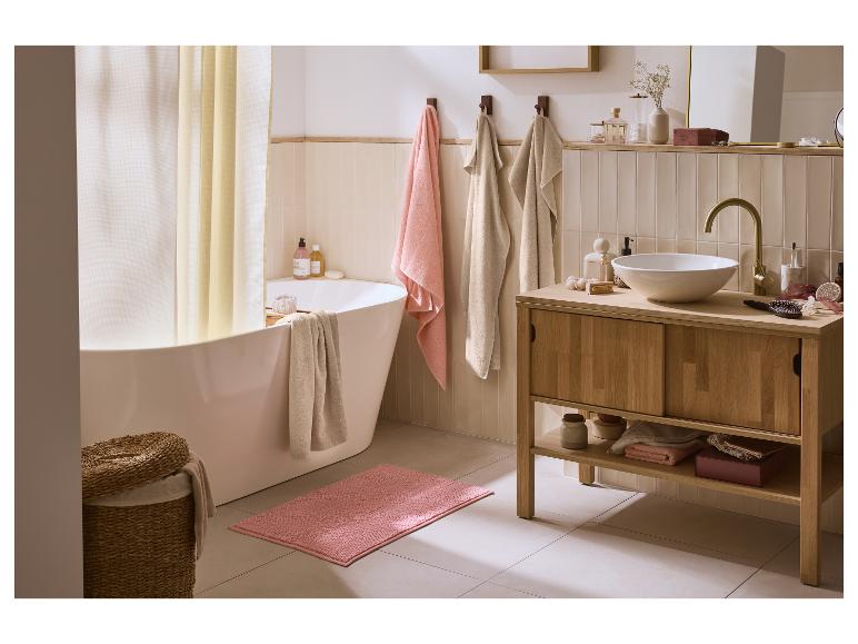 Badkamer met wit bad, houten wastafelmeubel en roze badmat.