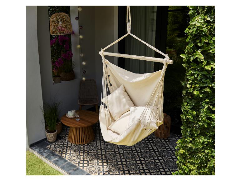 Stoffen hangstoel met kussens op een terras met patroontegels en planten.