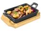 Geroosterd vlees met champignons, rozemarijn en ui in een zwarte pan op een houten plank.