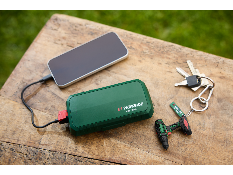 Groene powerbank laadt smartphone op, met sleutels en mini-boormachine sleutelhanger.