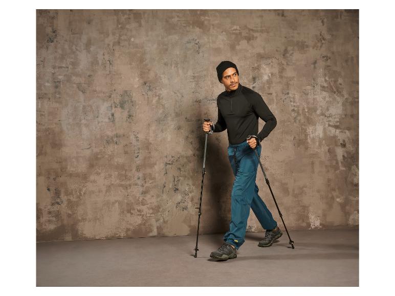 Man met wandelstokken en wandelschoenen loopt tegen een betonnen muur.