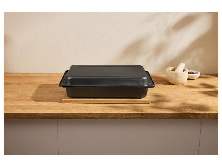 Zwarte braadslede met deksel op een houten tafel, met vijzel en kruiden.