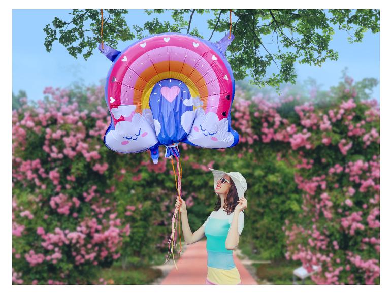 Vrouw met hoed en regenboogballon in een rozentuin.