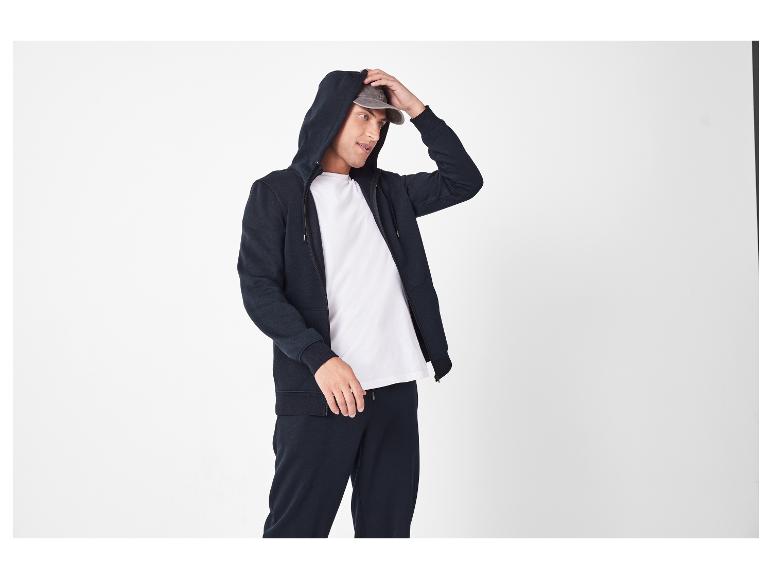 Man in donkerblauwe hoodie, wit T-shirt en bijpassende joggingbroek.