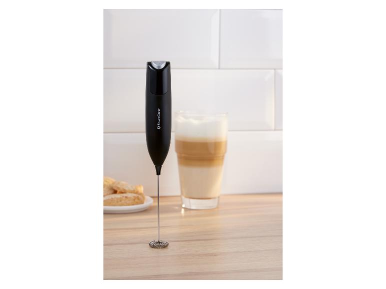 Zwarte melkopschuimer op een houten oppervlak naast een glas latte en koekjes