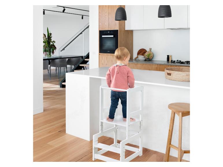 Een kind staat op een witte leertoren naast een modern keukeneiland.