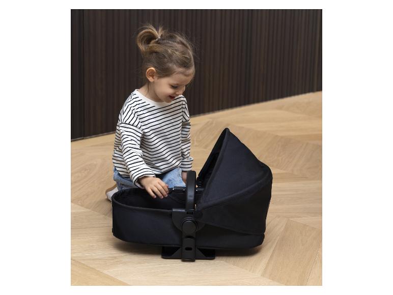Een kind speelt met een zwarte reiswieg.
