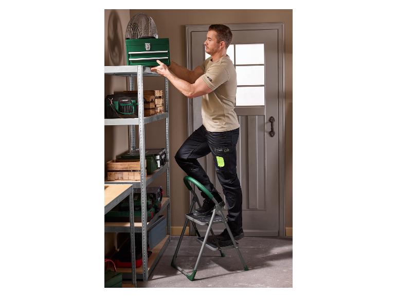 Man op ladder plaatst groene gereedschapskist op metalen rek.