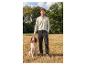 Man in shirt met lange mouwen en broek aait een hond buiten.